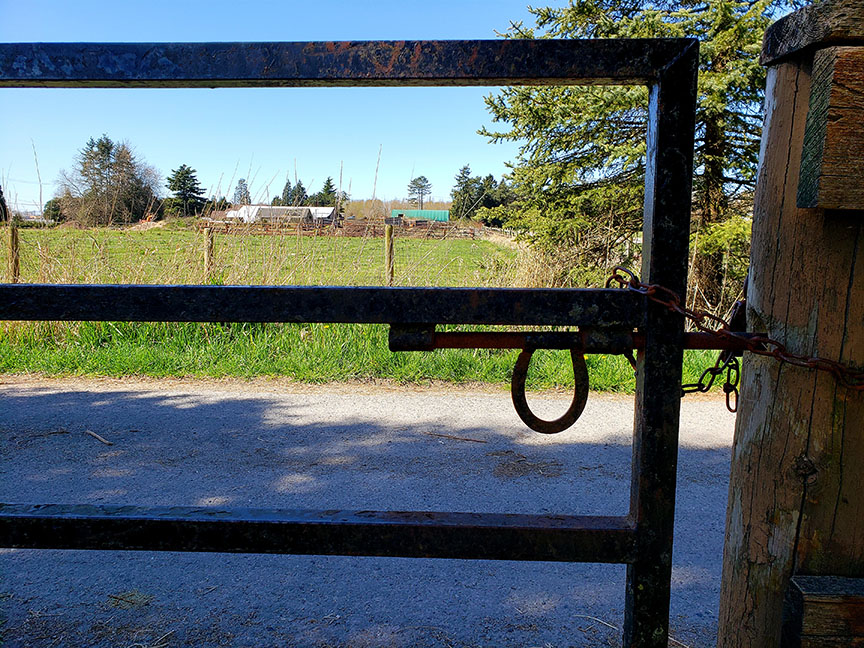photo of a horseshoe-shaped latch on a farm gate with fields and barns in the background