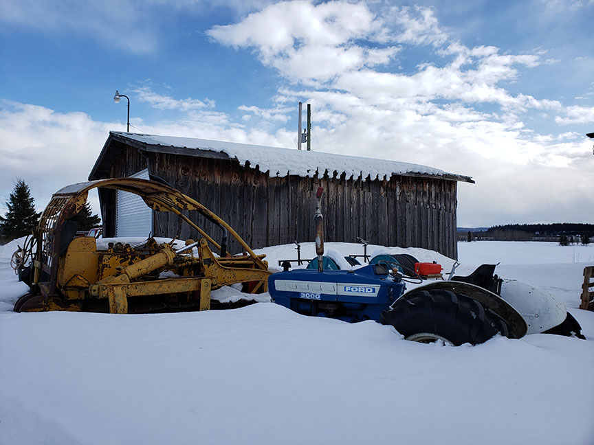 farm equipment buried in deep snow outside a barn