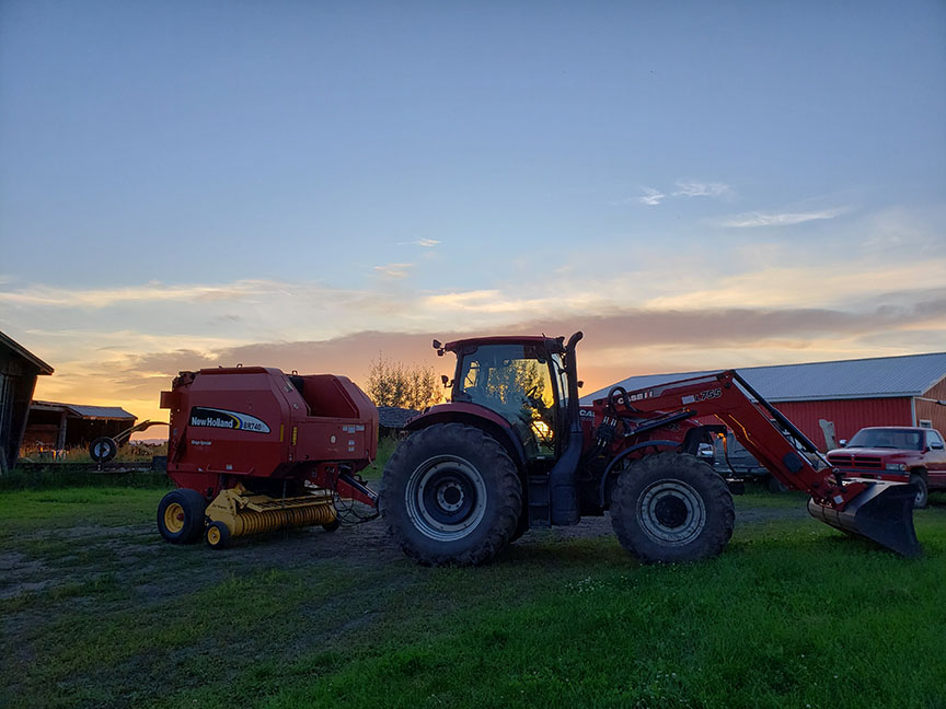 photo of a big red tractor in front of a red barn, at sunset