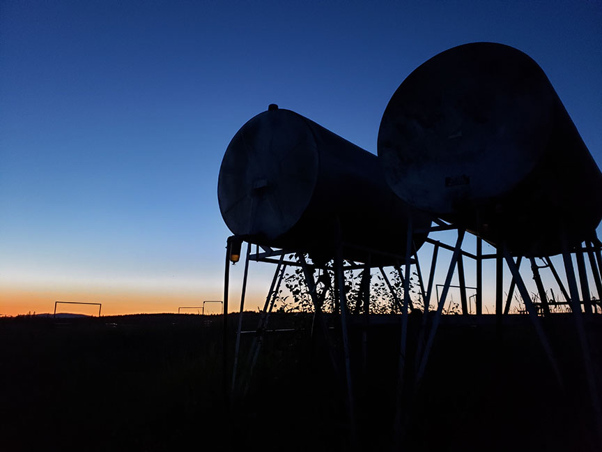 silhouette photo of two large fuel tanks on a ranch with the last legs of sunset in the background