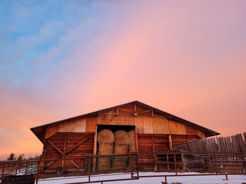soft pink and orange sunset above a tall hay shed surrounded by snow