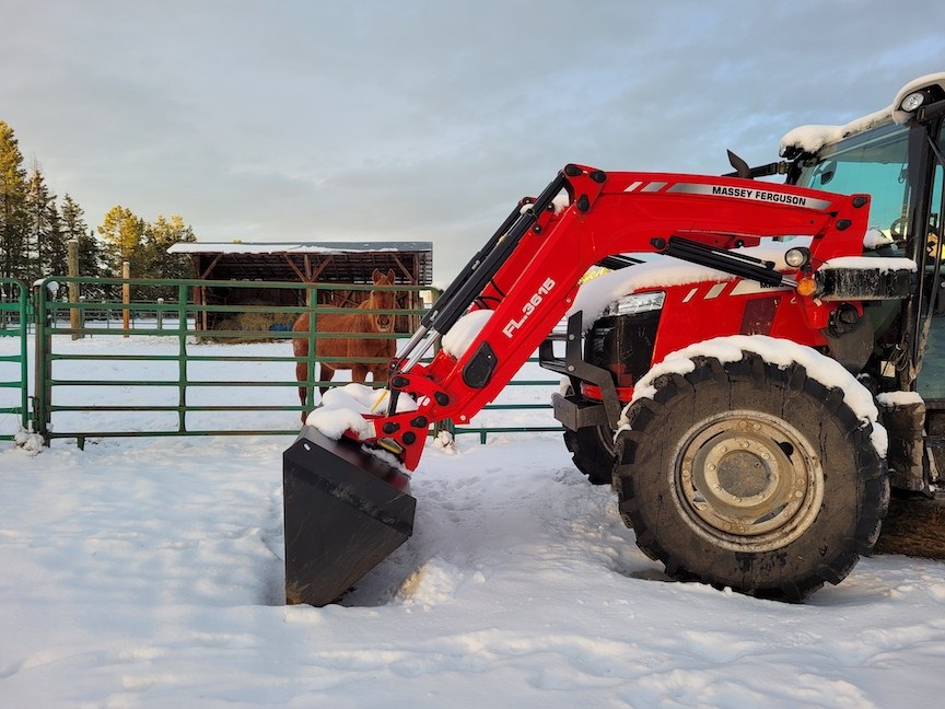 photo of a red tractor parked in snow, with a chestnut horse looking out from behind it between paddock fence rails
