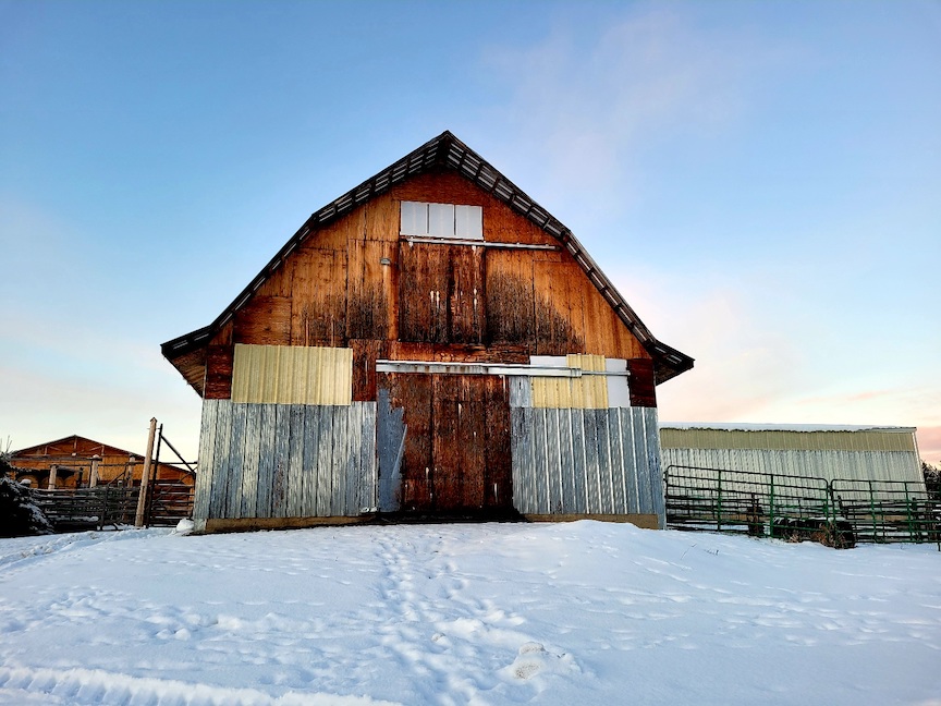 photo of a tall wooden barn with a sharply sloped roof, with snow in the foreground