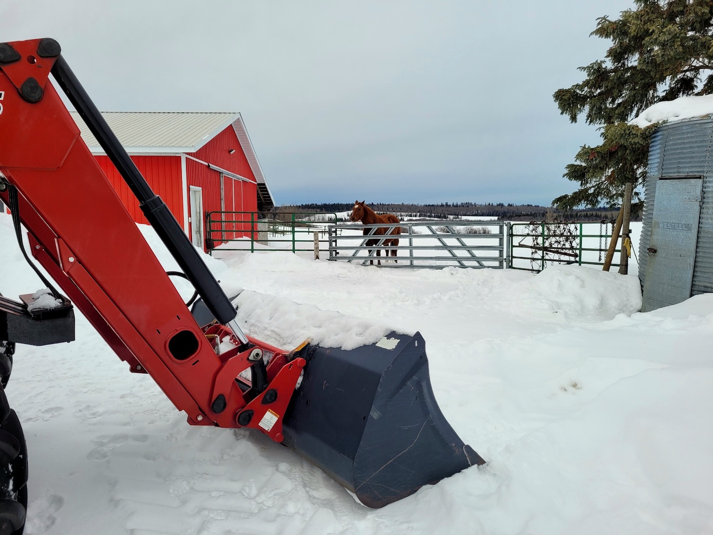 photo of a red tractor arm in front of a red barn, surrounded by snow