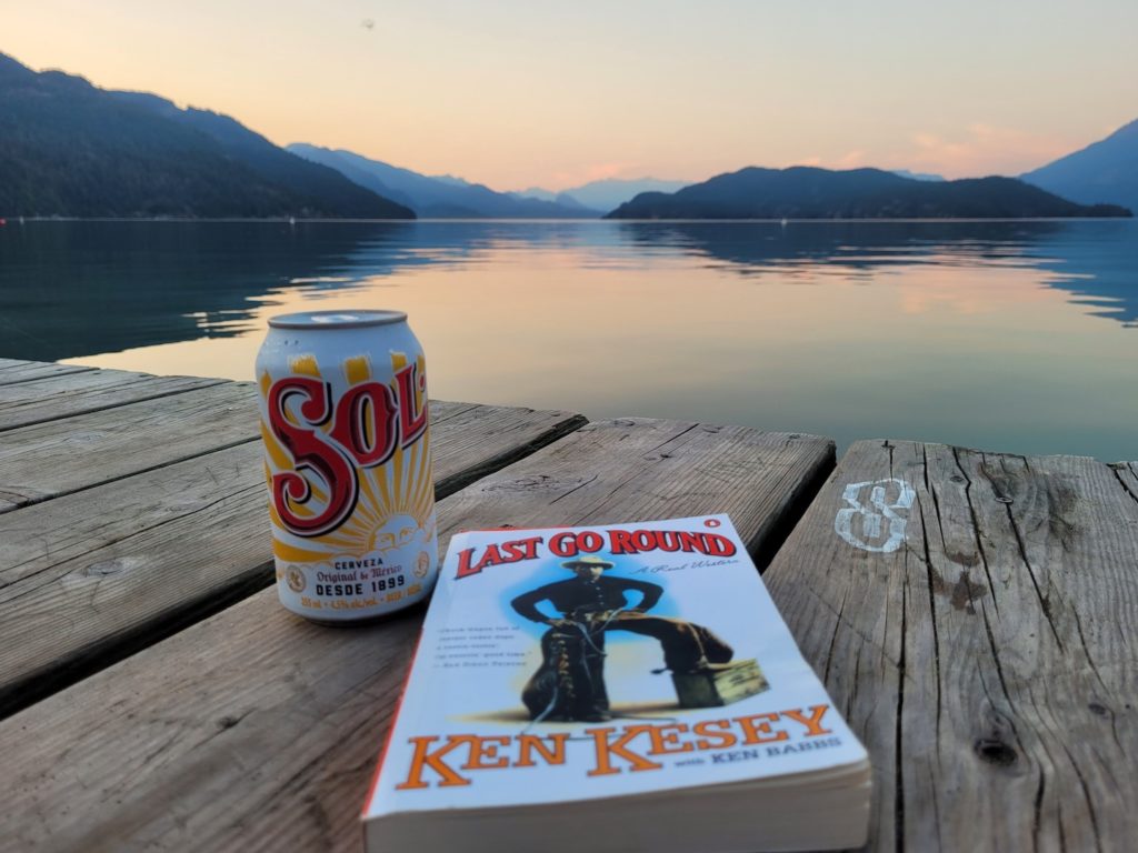 photo of the Last Go Round paperback on a dock with a can of Sol beer, a sunset over a lake in the background