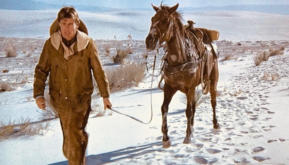 a scene from Bite the Bullet showing Jan-Michael Vincent walking a horse by its reins 