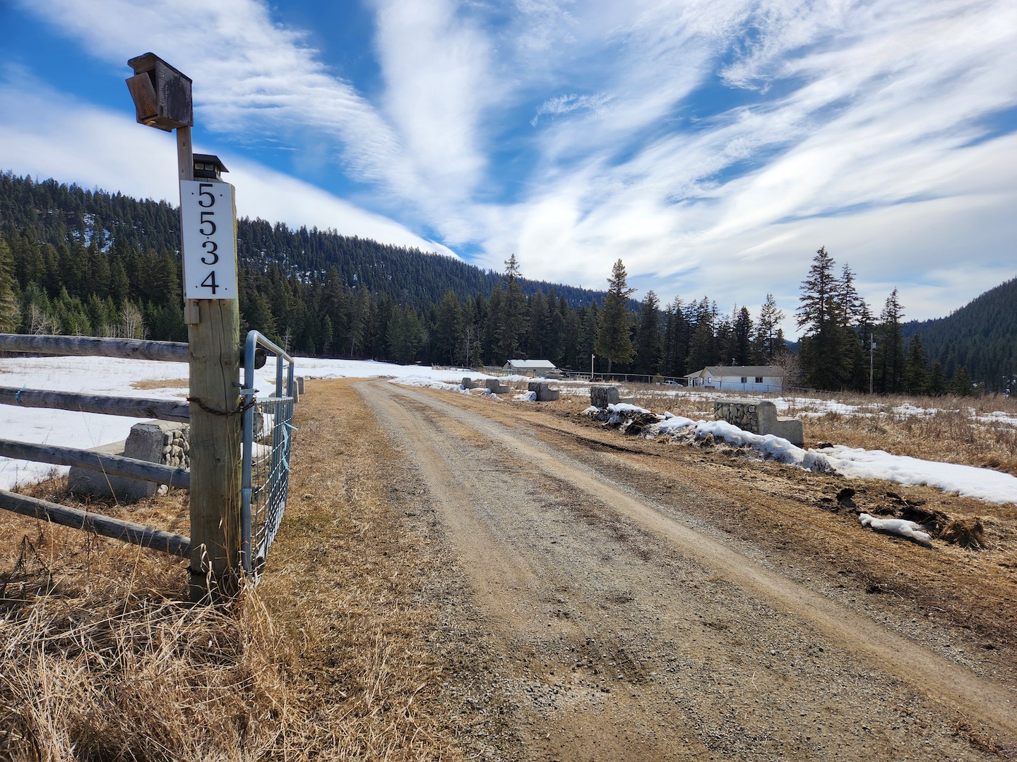 photo of a ranch driveway with snow melting in the distance
