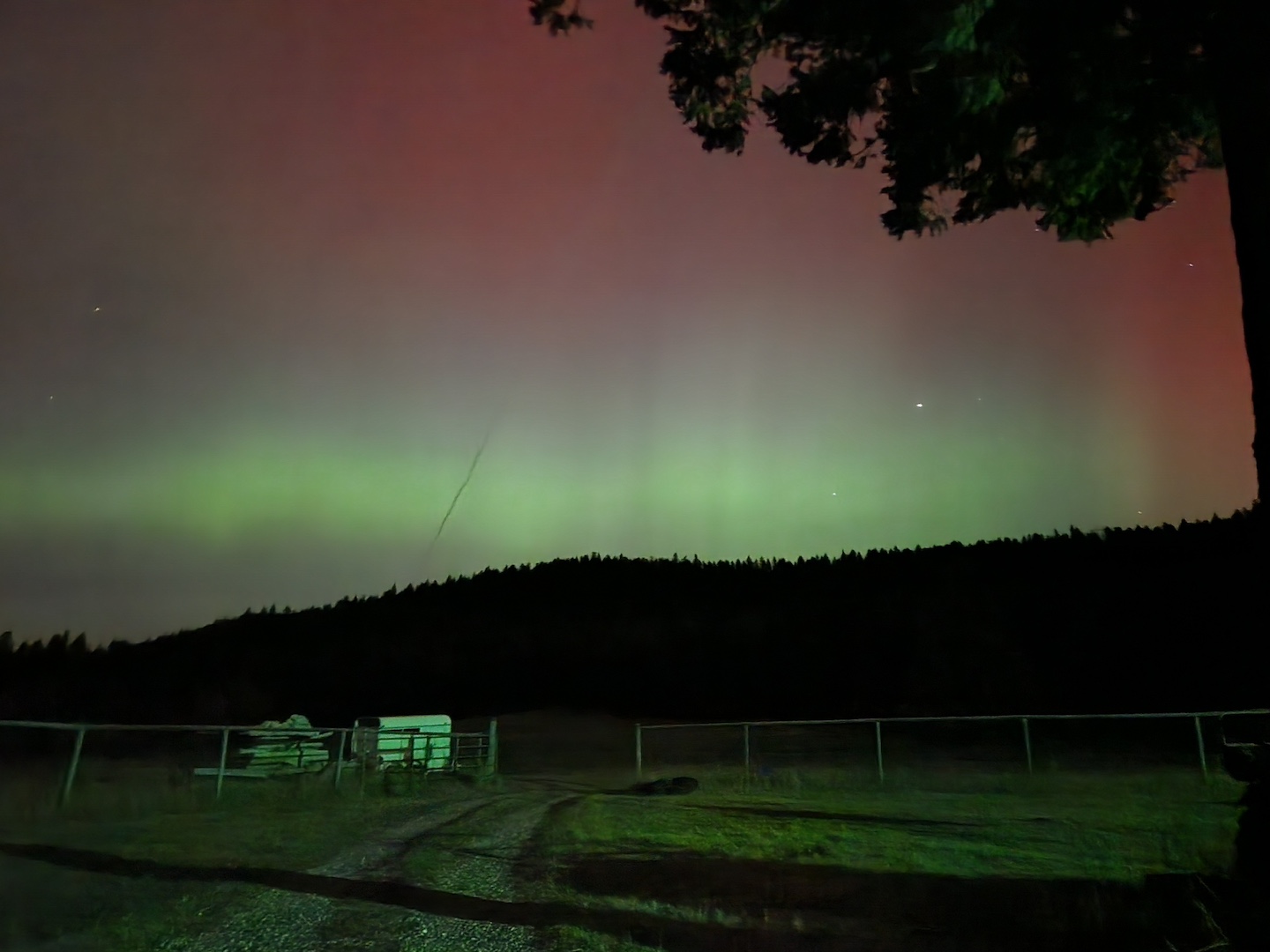 bright green and red northern lights over a dark, distant hill