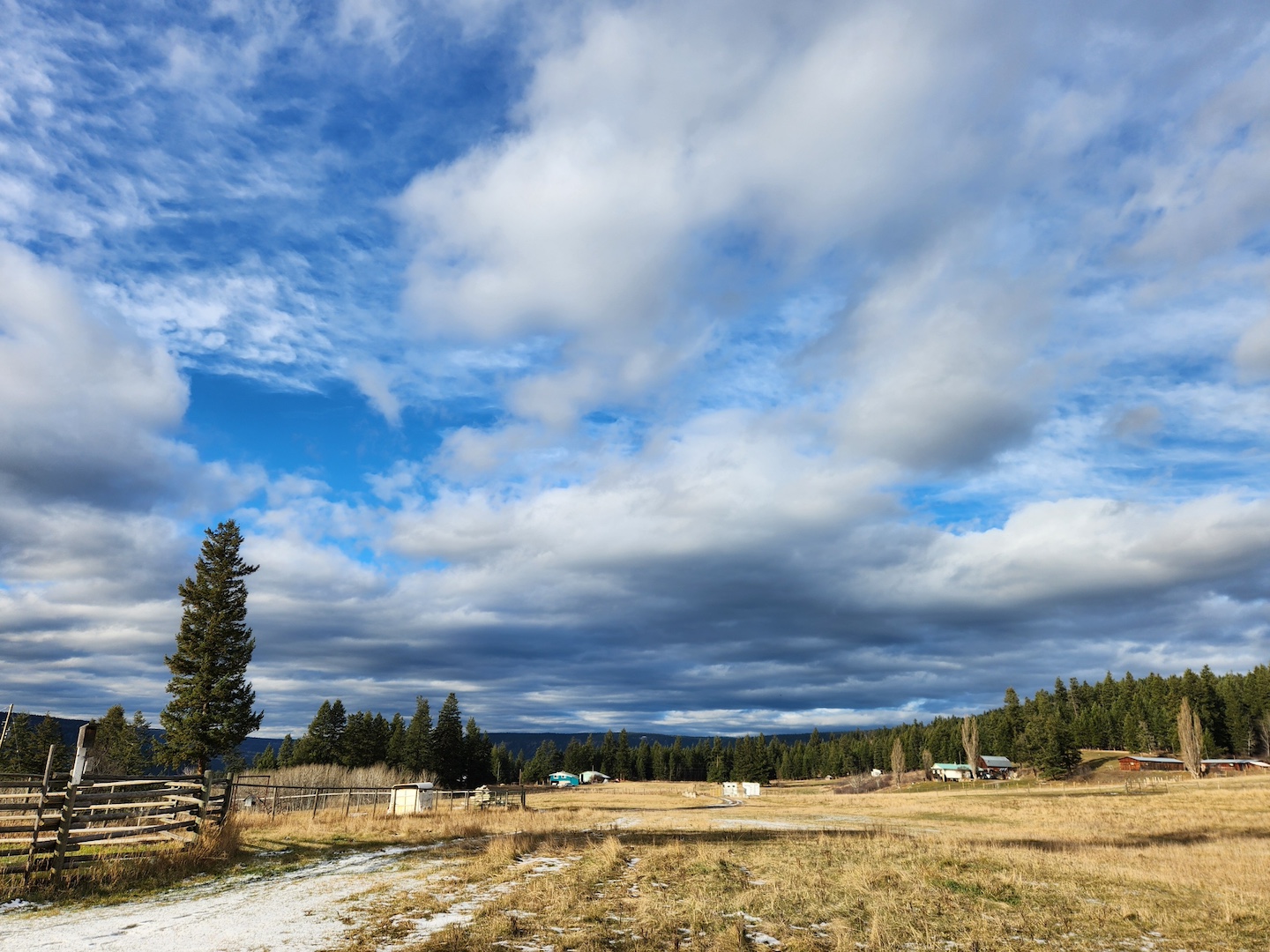 photo of a farm field in early winter, dead grass and a single patch of snow on the long driveway, blue sky overhead