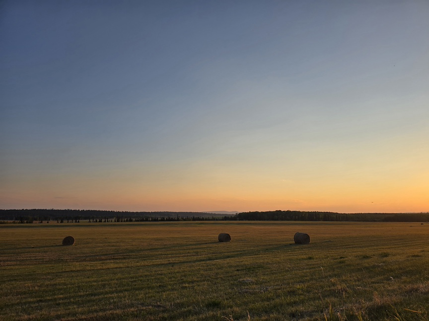a deep sunset over a hay field with scattered bales silhouetted by the low sun
