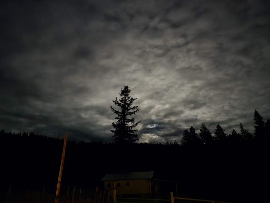 photo of the sky at night, clouds lit by the moon, over a barn