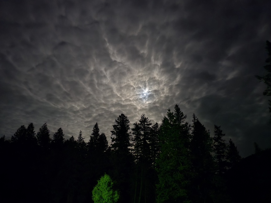 a dark moon surrounded by massive clouds in a night sky