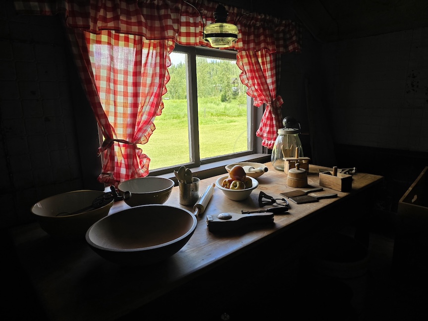 a window in a preserved pioneer home, with red gingham curtains and cooking tools laid out on the counter
